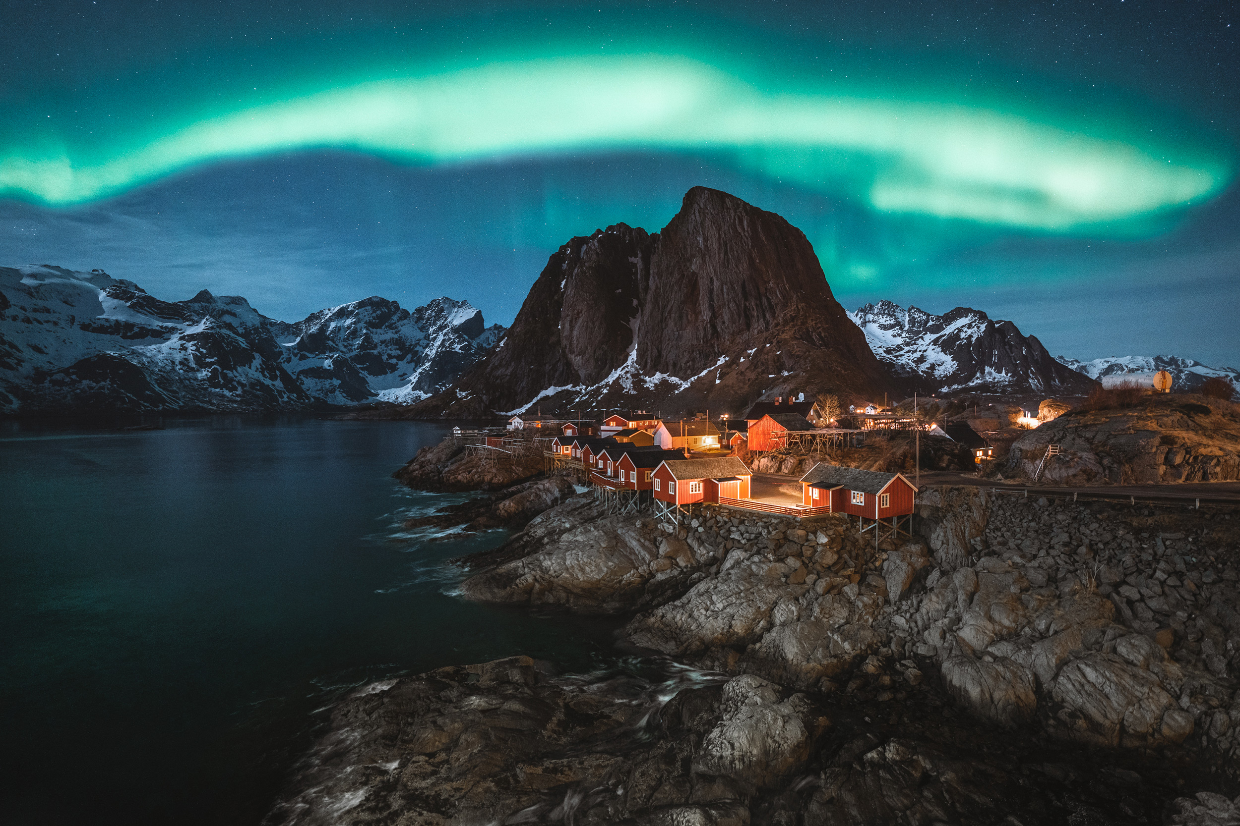 the-northern-lights-shimmering-above-a-group-of-huts-by-the-sea.jpeg
