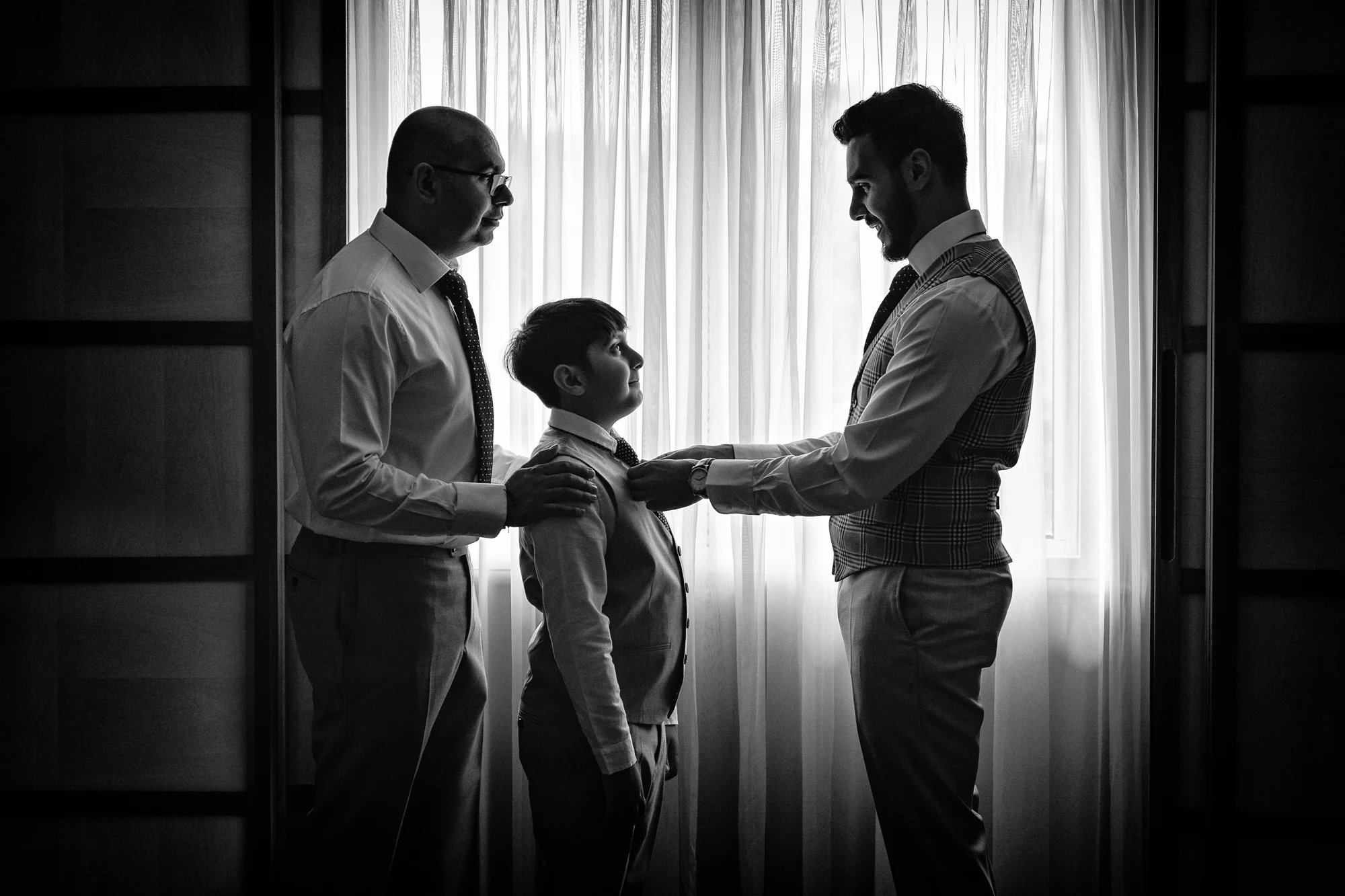 kate-hopewell-smith-sony-alpha-9-groom-adjusts-page-boy-tie-before-ceremony-as-father-looks-on.webp
