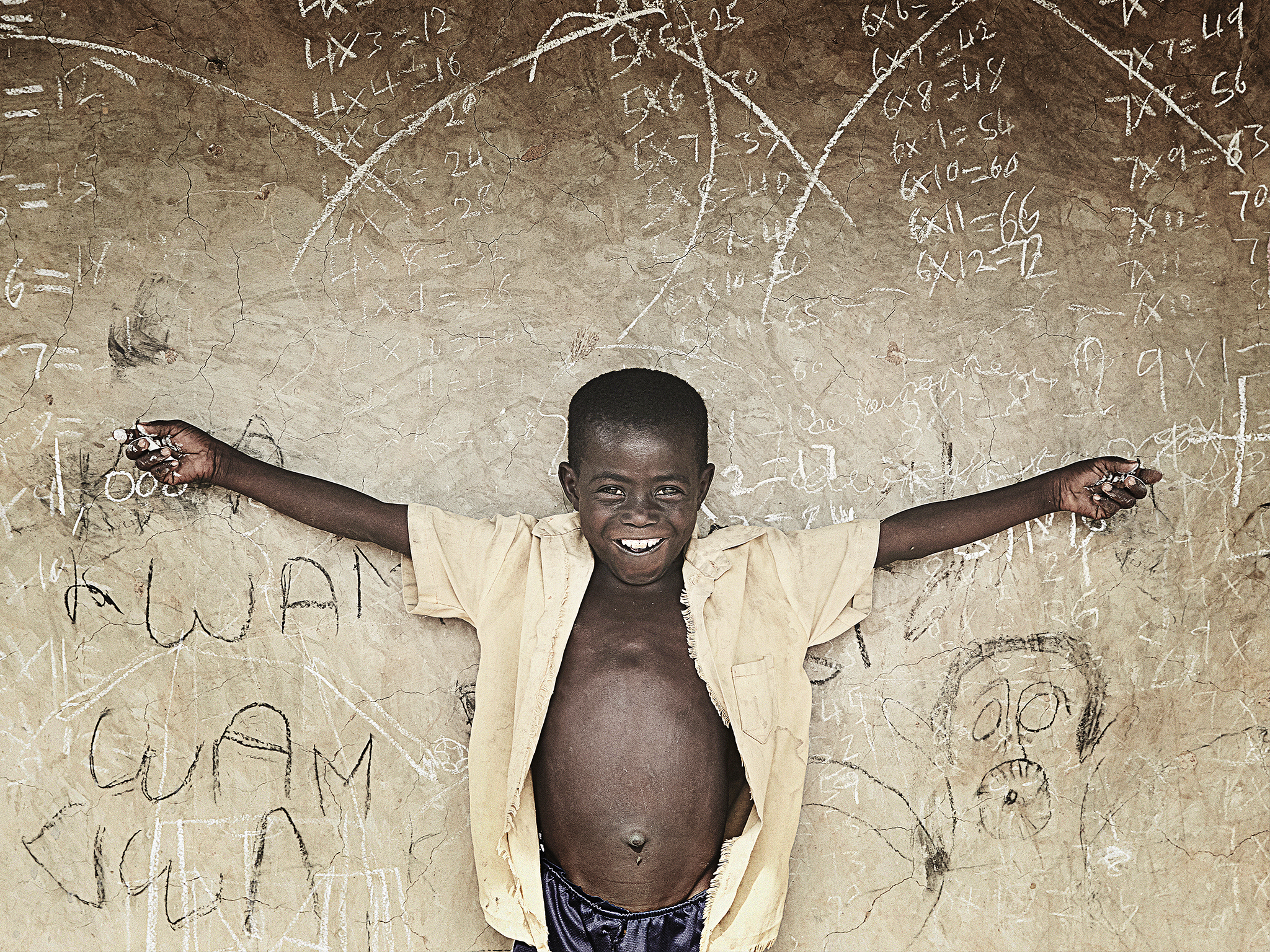 Ghanalainen lapsi poseeraa liitutaulun edessä.